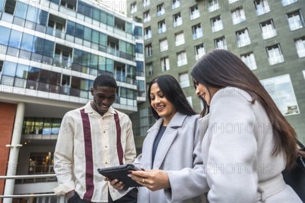 Diverse business professionals smiling and collaborating while reviewing data together on a touchscreen tablet outside an office building, demonstrating teamwork and modern communication