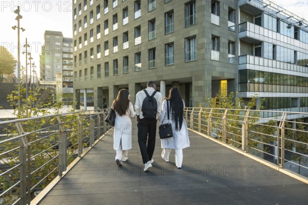Diverse business colleagues are walking away on an outdoor bridge, heading towards modern corporate buildings, symbolizing teamwork, progress, and urban professional life