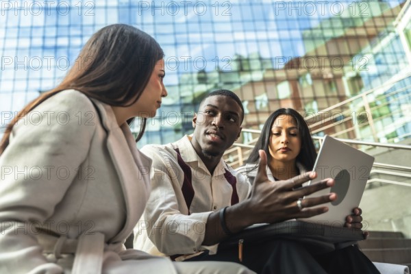 Diverse business team meets outdoors in an urban setting, sharing ideas over a laptop while discussing strategy, collaboration and remote communication for a startup project