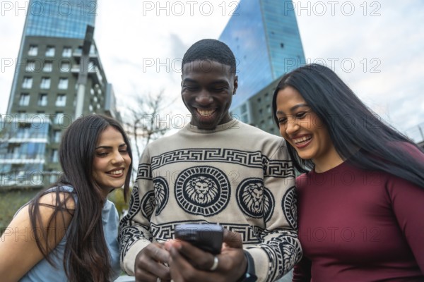 Diverse friends laughing and smiling while gathered on a city street, looking at a smartphone and sharing a joyful, casual moment of connection and social media fun