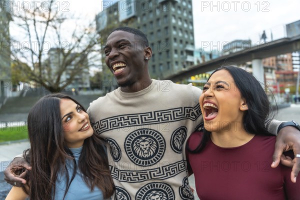 Three multiethnic friends laughing and embracing on a city street, sharing joyful, candid moments of connection and togetherness in an urban lifestyle scene