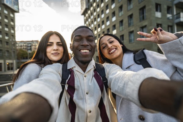 Three smiling multiracial friends enjoying an outdoor moment, capturing a joyful selfie together in an urban setting with modern buildings in the background