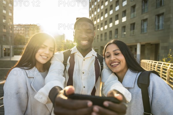 Group of diverse young adults smiling and having fun together while taking a selfie with a smartphone, capturing happy moments in an urban setting with golden hour light