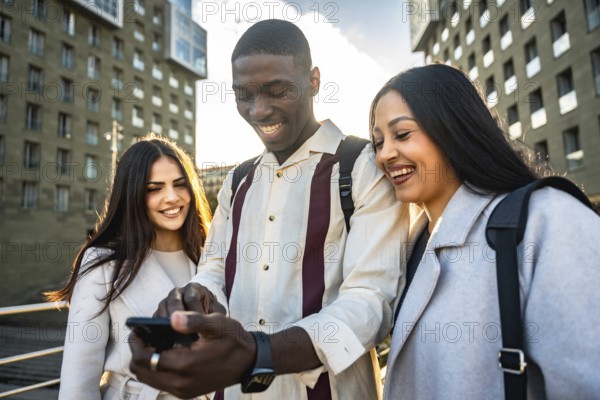 Diverse group of young friends laughing and sharing smartphone content outdoors in a sunny urban setting, enjoying casual connection, social media browsing and togetherness