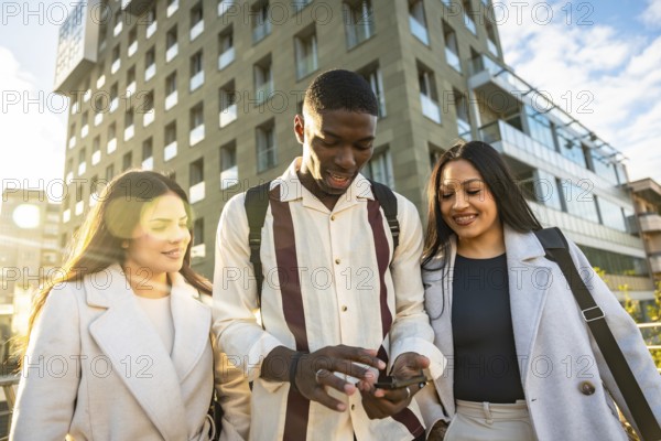 Young diverse friends walking in the city, smiling and gathered around a smartphone, sharing content and enjoying sunny urban life, connection and casual conversation