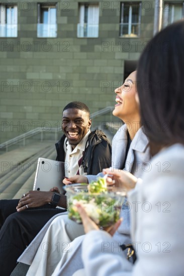 Diverse group of friends or colleagues enjoying a happy moment together outdoors, laughing and eating a healthy salad during a casual lunch break in the city
