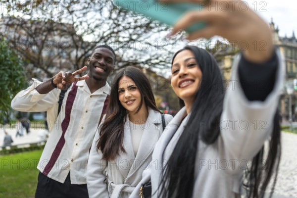 Happy diverse friends smiling and posing for a cheerful selfie with a smartphone outdoors in a city park, capturing a candid moment of youthful fun, connection, and travel memories