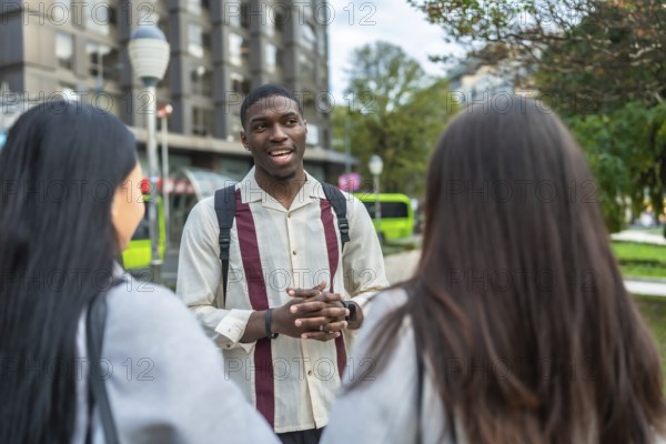 Young diverse friends standing outdoors in an urban setting, conversing casually on a sunny day, representing communication and social interaction in a multiethnic group