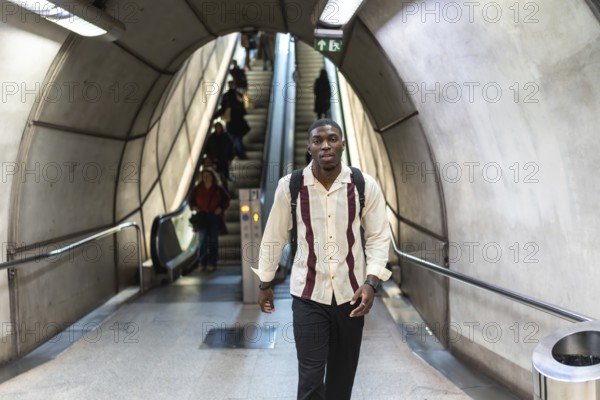 Young man with backpack walking confidently through a modern subway tunnel past escalators and commuters, capturing daily urban commute, public transit and purposeful movement