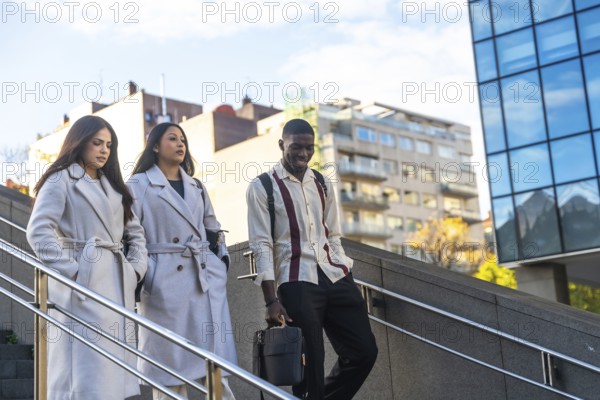 Three diverse business colleagues descending outdoor stairs, walking together after work or during a break, depicting office life, teamwork, and urban professionals