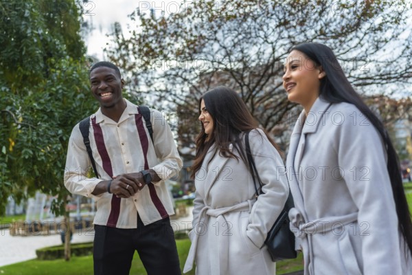 Multiracial young adults walking together in an urban park, smiling and happily conversing, showing friendship and a strong sense of community while connecting outdoors