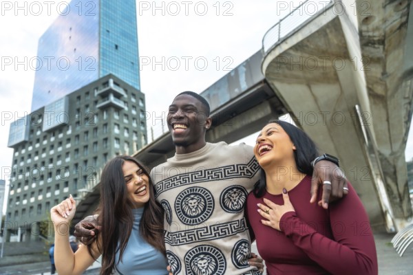 Cheerful diverse group of young adults standing closely together, smiling, laughing, and enjoying a moment of genuine friendship and happiness in a modern city environment