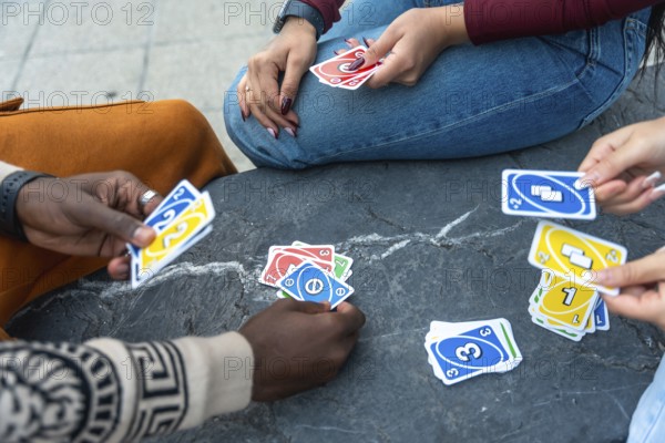 Diverse people gathering outdoors, playing a popular card game, throwing cards onto the stone surface, sharing a moment of leisure, fun, community, and friendship