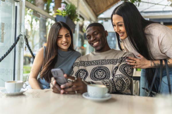 Multi ethnic friends enjoying coffee, sharing a cheerful moment while looking at a smartphone screen, smiling and laughing together inside a modern cafe