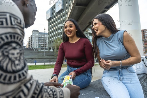 Diverse group of young adult friends enjoying a casual game of cards and laughing together in an urban setting, sharing moments of leisure and connection