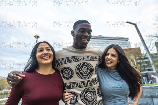 Diverse group of three happy young friends, a black man embracing two hispanic women, walking together and laughing cheerfully in an urban setting with the space needle visible in the background