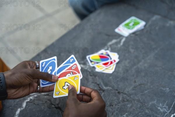 Hands holding a colorful fan of playing cards over a stone table during a casual indoor card game, conveying fun, friendly competition, strategy, and relaxed social bonding