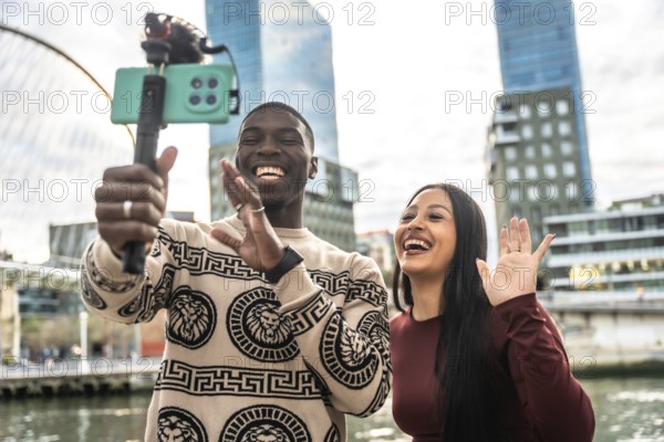 Happy young multiracial couple creating content with a smartphone on a selfie stick, streaming live and sharing their fun city adventure with followers