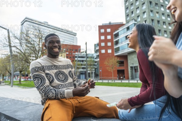 Group of diverse young adult friends laughing, smiling, and enjoying a casual urban leisure moment together, sitting outdoors in a modern city setting