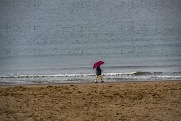 Person with red umbrella walking along the beach, calm sea in the background, winter break, on Zeedijk-Knokke, beach promenade in Knokke-Heist, beach walkers with umbrella when it rains, dreary winter day, Belgium