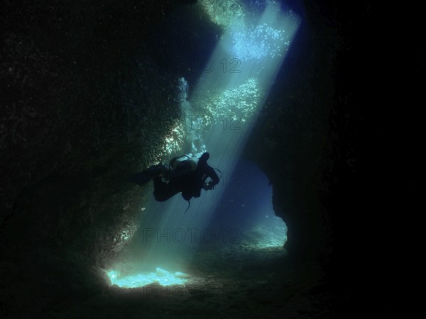 A diver floats through a mystical underwater cave, flooded with blue light. Fraskeric dive site, Stoja, Pula, Croatia, Mediterranean