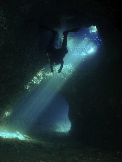 A dark cave is explored by a diver who is surrounded by dramatic rays of light. Fraskeric dive site, Stoja, Pula, Croatia, Mediterranean