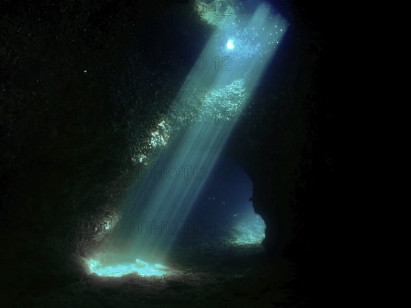 Sun rays illuminate the interior of a dark underwater cave with blue light reflections. Fraskeric dive site, Stoja, Pula, Croatia, Mediterranean Sea