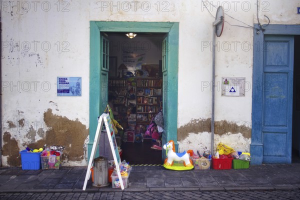 Landscape image of a shop front in Arrecife, Lanzarote. Two wide open doors offer a view of the sales room, with toys and colorful posters in front of them. There is a sign on the façade that says AYUDA PARA AYUDAR, Arrecife Lanzarote