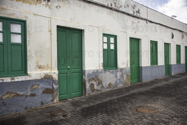 Long, single-storey row of houses in Arrecife, Lanzarote, taken from an oblique perspective. Broken plaster and green doors along a paved road that draws the eye into the depths, Arrecife Lanzarote