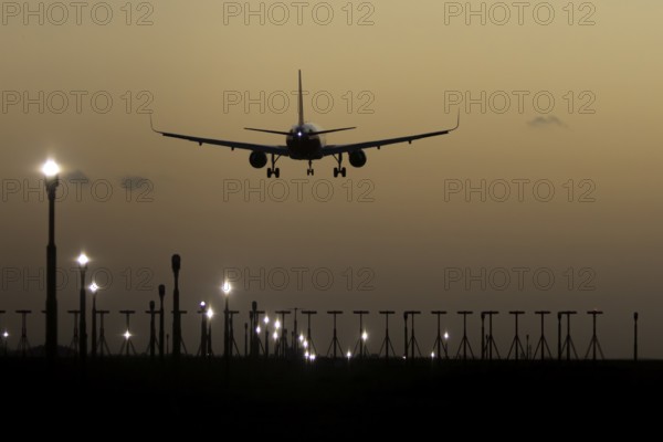 Airbus 320 commercial passenger airliner jet aircraft in flight on approach to land over runway lights at sunset at London Stansted airport, Essex, England, United Kingdom