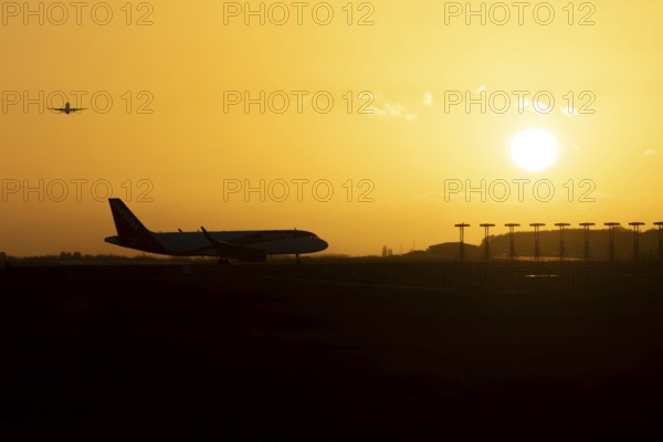 Airbus commercial passenger airliner jet aircraft taking off in flight with another plane on the taxiway at sunset at London Stansted airport, Essex, England, United Kingdom