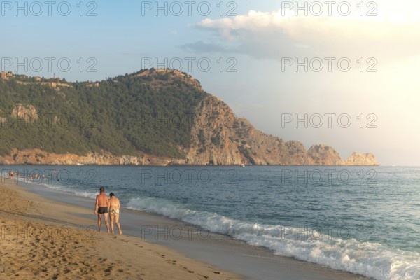 A couple walk along an empty Cleopatra Beach at sunset in the Turkish holiday resort town of Alanya on the Mediterranean coast of Turkey, the Turkish Riviera