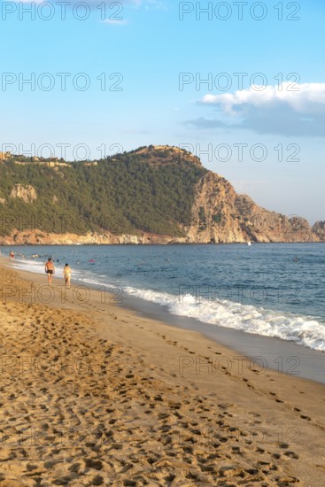 A couple walk along an empty Cleopatra Beach at sunset in the Turkish holiday resort town of Alanya on the Mediterranean coast of Turkey, the Turkish Riviera