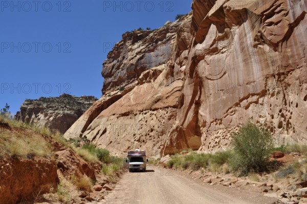 A camper drives along a dirt road in a canyon with red rock walls, Capitol Reef National Park, Utha, USA