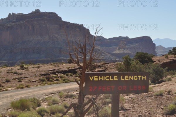 Desert landscape with vehicle length road sign and rocky mountain range in the background, Capitol Reef National Park, Utha, USA
