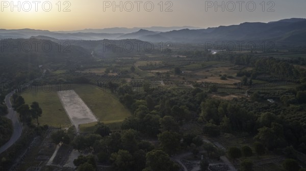 Ancient stadium in the morning backlight, wide landscape at sunset with hills and a large rectangular field in the foreground, drone shot, archaeological site, Ancient Olympia, Peloponnese, Greece