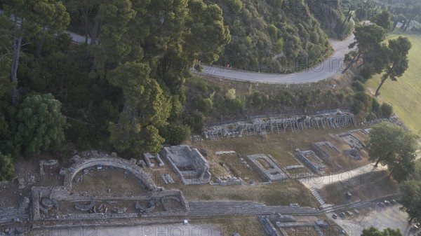 Old theatre and ruins next to a road surrounded by dense nature, drone shot, archaeological site, Ancient Olympia, Olympia, Peloponnese, Greece