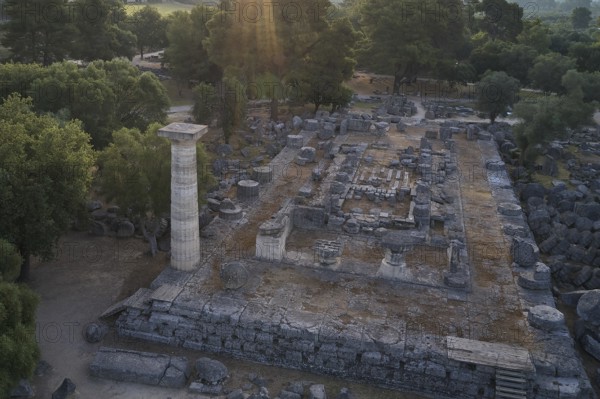Temple of Zeus in backlight, archaeological remains with stone column and trees, in light of the setting sun, drone shot, archaeological site, Ancient Olympia, Olympia, Peloponnese, Greece