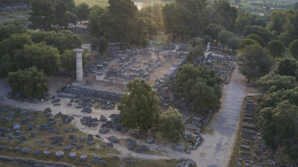 Temple of Zeus in backlight, ancient ruins surrounded by trees, with a single stone pillar amidst the ruins, drone shot, archaeological site, Ancient Olympia, Olympia, Peloponnese, Greece