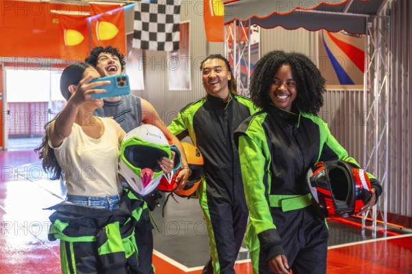 Diverse group of young adult friends wearing racing suits and holding helmets, posing for a cheerful selfie while enjoying a fun karting activity together at an indoor track