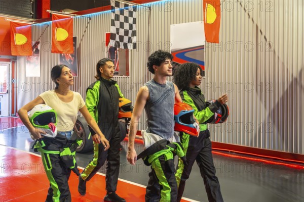 Group of diverse gen z friends holding racing helmets and walking in an indoor karting facility, preparing for an exciting go kart race, symbolizing youth, entertainment, and connection