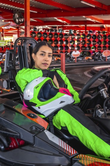 Young woman in a bright green racing suit holding a helmet and sitting in a go kart, ready for a race or practicing on the track, showcasing passion for motorsport