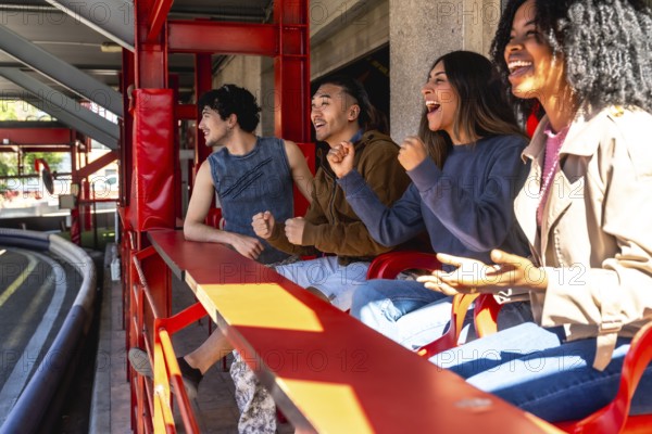 Diverse group of young adult friends are enthusiastically watching and cheering a karting race from the sidelines, expressing excitement and support for the participants