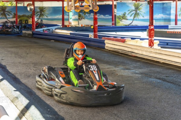 Man in orange helmet and green jumpsuit powering a go kart around a race track, pushing speed and focus in outdoor karting competition, thrill and recreational racing action