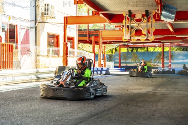 People wearing helmets and green racing suits driving go karts around an outdoor track, enjoying the thrill of speed and competition during a sunny day