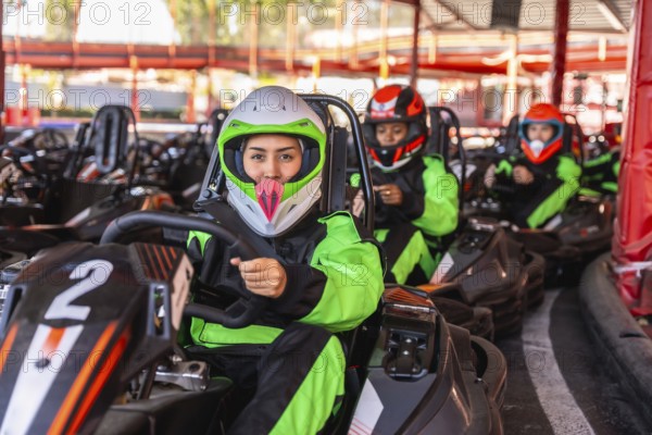 Young women in helmets and racing suits sit in go karts on an outdoor track, lined up and ready to start a fun, competitive karting session with friends and excitement