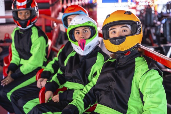 Young diverse friends in helmets and racing suits sit in go karts on an indoor track, ready and focused for a fast, fun, adrenaline filled karting race together