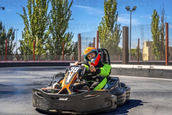 Young man in helmet and racing suit zooming a go kart on an outdoor asphalt track, enjoying speed and competition on a sunny day during a weekend karting session
