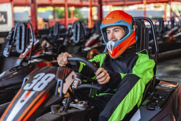 Man wearing an orange helmet and racing suit, sitting inside a go kart with the number 38, holding the steering wheel and preparing to race on a karting track