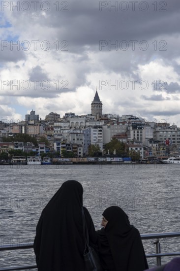Istanbul, Turkey. September 18th 2025. Muslim women beside the Golden Horn with the Galata Tower rising above the European side of Istanbul, Turkey